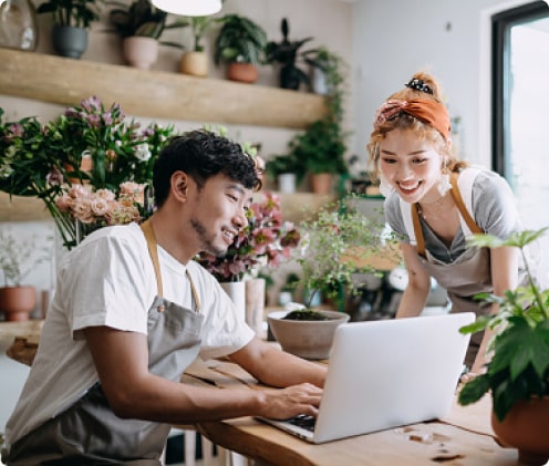 A young man and a young woman in a plant store look at a laptop computer screen together.