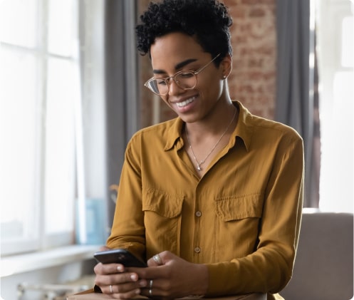 A young woman smiles as she looks at the screen of the phone she is holding.