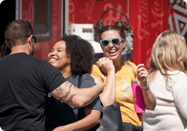 A group of young people laughing and smiling together on a sunny day outdoors.