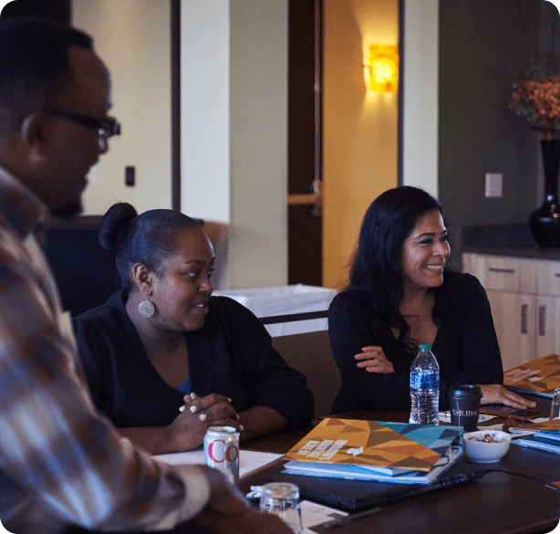 Three Better Business Bureau employees, two women and one man, sit at a conference room table, working and laughing together.