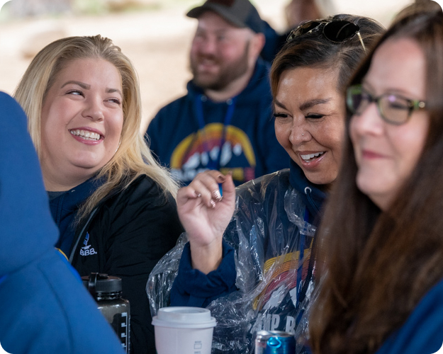 Better Business Bureau colleagues sit together at an outdoor event, laughing and having fun.